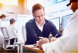 A gentleman working with another person to understand drug plans with other employees in their cubicles