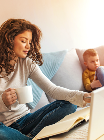 A young mother looking  through her Express Scripts Canada health benefits package while sitting on the couch with her son playing in the background