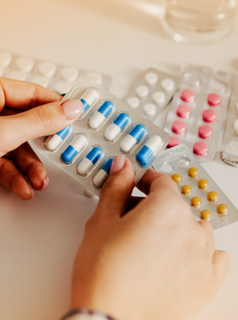 A hand holding a pack of pills with other pills in the background