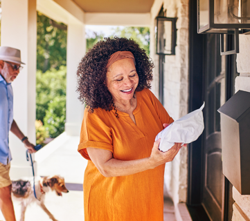 A smiling woman holding a package while standing on porch in front of her house