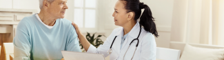 A young asian female physician with her hand on an older gentlemans shoulder explaining medications