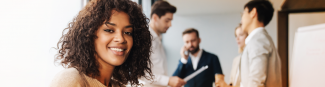 Une jeune femme noire souriante est assise devant des clients qui se tiennent debout.