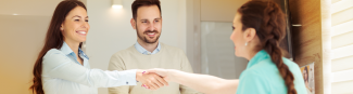 A young woman, standing beside a man, shaking hands with a dental receptionist 