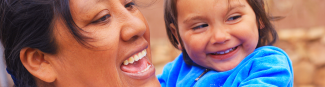 A close crop of an Indigenous mother holding a smiling child