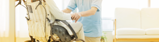 Close crop of young health care professional in a blue shirt kneeling in front of patient sitting in a wheelchair 